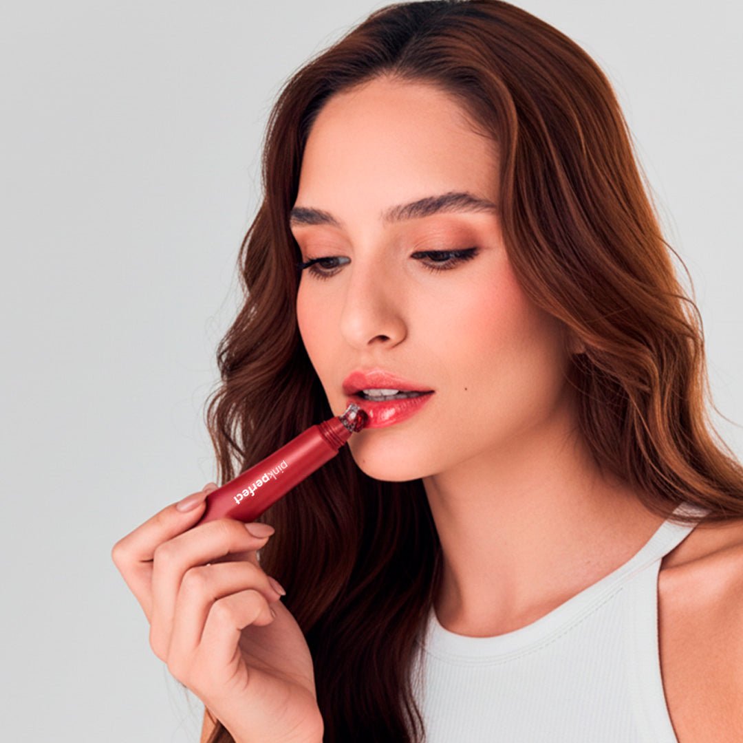 Mulher aplicando gloss labial vermelho, maquiagem natural, foco em skincare facial.
