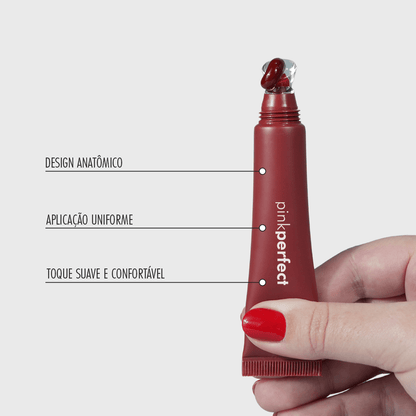 Mão segurando lip balm vermelho com aplicador anatômico e textura cremosa para cuidados labiais.